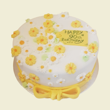 A white birthday cake decorated with yellow flowers and a "Happy 90th Birthday" message.